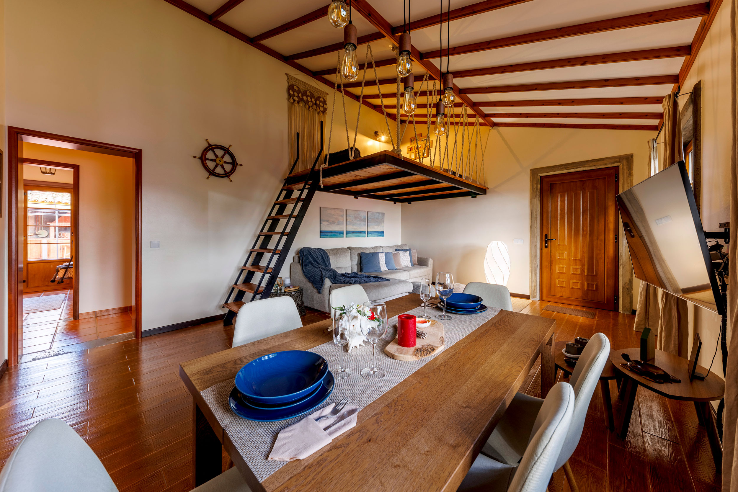 Wide view of the living room with a wooden dinner table, a soft beige sofa and a loft at Refúgio Azores stay in Terceira.